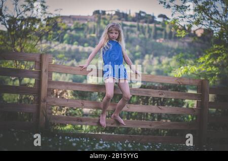 Adorable petit enfant assis à la clôture en bois dans la nature verte dans la magnifique romantique Toscane italienne Banque D'Images