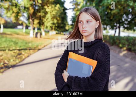 Fille école parc d'été mains carnets manuels livres. Arrière-plan route arbres vert herbe. Espace libre pour le concept de texte étudiant l'institut scolaire Banque D'Images