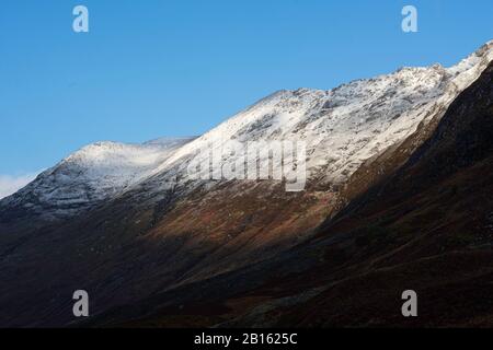 Paysage majestueux de l'Ecosse.ciel bleu clair au-dessus de la crête enneigée de montagne avec des pentes éclairées par la lumière du soleil du matin et des ombres profondes dans la vallée au-dessous.tr Banque D'Images