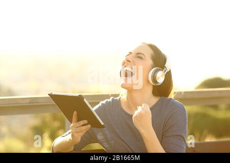 Une femme excitée tenant une tablette et portant un casque hurlant et célébrant les bonnes nouvelles Banque D'Images