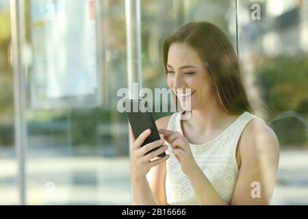 Bonne jeune femme qui a vérifié le smartphone en attendant que le bus arrive Banque D'Images