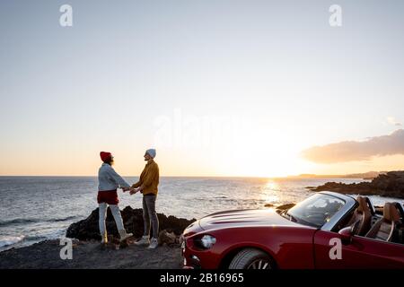 Couple profitant de belles vues sur l'océan, ensergeant ensemble près de la voiture sur la côte rocheuse, vue large du côté avec espace de copie sur le ciel Banque D'Images