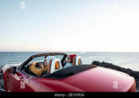 Couple conduisant une voiture convertible, en voyageant près de l'océan sur un coucher de soleil, vue de l'arrière. Bonnes vacances et voyage en voiture concept Banque D'Images