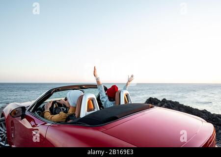 Couple conduisant une voiture convertible, en voyageant près de l'océan sur un coucher de soleil, vue de l'arrière. Bonnes vacances et voyage en voiture concept Banque D'Images