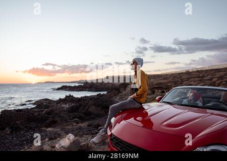 Portrait de style de vie d'un homme sur la côte rocheuse au coucher du soleil, voyageant avec une femme en voiture Banque D'Images