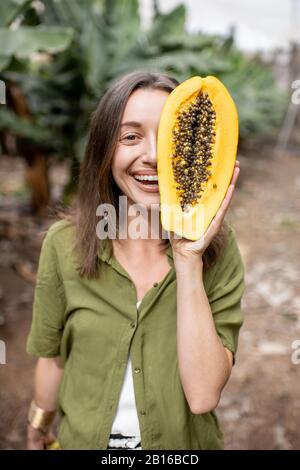 Gros plan portrait d'une jeune femme cachant son visage derrière des fruits de papaye tranchés à l'extérieur sur le fond vert. Concept de soins de la peau et de bien-être Banque D'Images