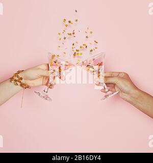 Célébration et vacances. Deux mains tenant des verres à vin avec de l'or confetti sur fond rose Banque D'Images