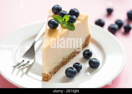 Cheesecake Slice Classique Servi Avec Des Bleuets Frais Et De La Feuille De Menthe Sur La Plaque Blanche, Fond Rose. Savoureux Dessert Sucré. Gâteau Crémeux Banque D'Images