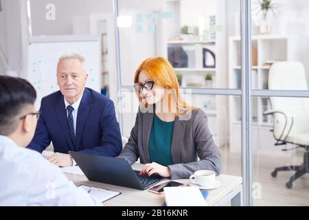 Portrait de deux responsables RH interviewant un jeune homme asiatique pour un poste au bureau, espace de copie Banque D'Images