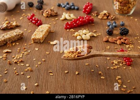 Spatule en bois au-dessus de la table avec de la granola à côté des baies, des noix et des barres de céréales sur fond en bois Banque D'Images