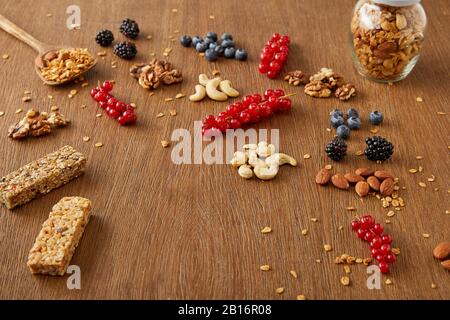 Bocal de granola à côté de baies, noix, barres de céréales sur fond de bois Banque D'Images