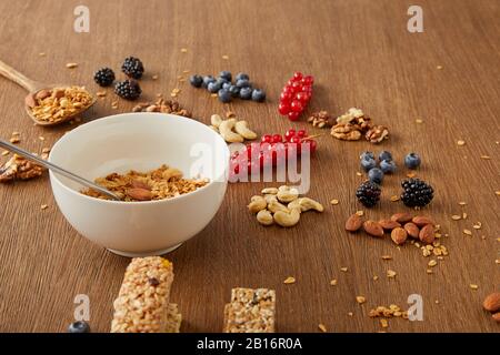 Bol avec la granola à côté des baies, des noix et des barres de céréales sur fond en bois Banque D'Images