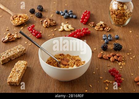 Bol et bol avec la granola à côté des baies, noix, barres de céréales sur fond de bois Banque D'Images