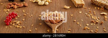 Spatule en bois avec granola à côté de groseilles, noix et barres de céréales sur fond en bois, vue panoramique Banque D'Images