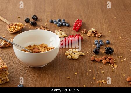 Bol avec la granola à côté des bleuets, des groseilles, des noix, des amandes, des noix de cajou sur fond de bois Banque D'Images