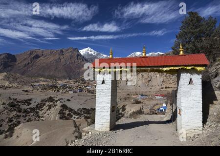 Porte En Pierre Bouddhiste Avec Toit Rouge Avec Des Pics De Neige Lointains Et Des Paysages Du Ciel Bleu Sur Le Circuit Annapurna Randonnée Trek Au Népal Himalaya Montagnes Banque D'Images