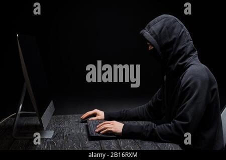 pirate dans le capot regardant le moniteur d'ordinateur avec un écran vide en noir Banque D'Images