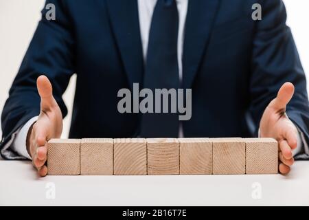 vue courte de l'homme d'affaires mettant les mains sur la surface avec des cubes de bois isolés sur blanc Banque D'Images