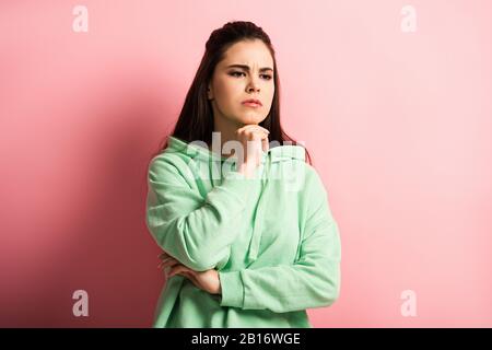 bouleversée, la fille réfléchie tenant la main près du menton tout en se tenant sur le fond rose Banque D'Images