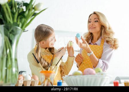 foyer sélectif de la mère heureuse et de la fille tenant des pinceaux et des oeufs de pâques peints Banque D'Images