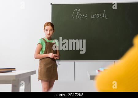 foyer sélectif de triste écolière debout près de tableau de surveillance avec lettrage de travail de classe Banque D'Images