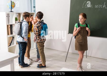 des écoliers cruels commérages et rire près de la jeune fille intimidée debout en classe Banque D'Images