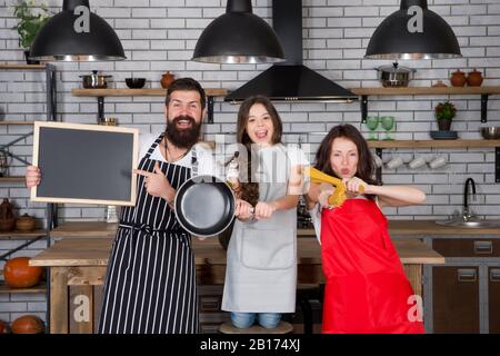 cuisine drôle. famille sympathique dans la cuisine. cuisine saine à la maison. chef cuisinier pour les enfants, dîner avec les parents. faites tout ensemble. gagnants du quotidien. La mère et le père cuisiniers avec la fille. Bonne journée familiale. Banque D'Images