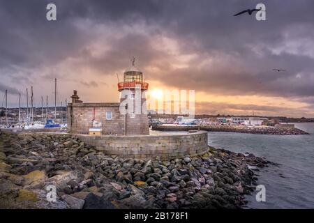 Phare de Howth avec des mouettes volantes au beau coucher du soleil. Bateaux à voile et bateaux à voile dans le port, Dublin, Irlande Banque D'Images