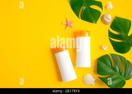Les bouteilles de crème solaire blanches se moquent sans étiquettes, feuilles tropicales et coquillages sur fond jaune. Protection contre le soleil et concept de soins de la peau. Couche plate, dessus Banque D'Images