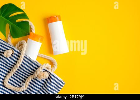 Flacons de lotion de bronzage sans étiquettes, sac de plage rayé et feuille tropicale et sur fond jaune. Vue sur le dessus, plat. Soins de la peau d'été prod cosmétique Banque D'Images