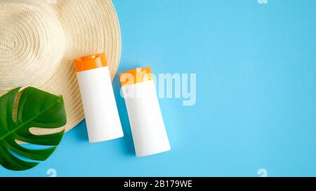 Crème solaire hydratant des bouteilles sans étiquette sur fond bleu avec chapeau de plage et feuille tropicale verte. Vue sur le dessus, plat. Le décomposent l'été et Banque D'Images