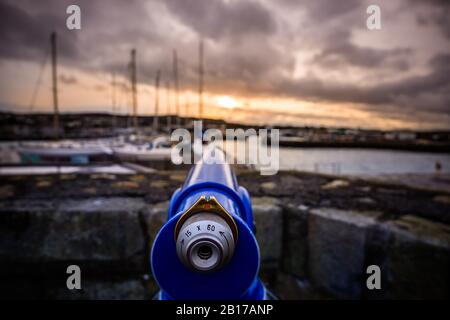 Focalisation sélective sur le télescope bleu au port de Howth avec des yachts flous et des couchers de soleil en arrière-plan, Dublin, Irlande Banque D'Images