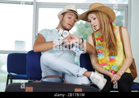 jeunes touristes assis au salon de l'aéroport et regardant la montre Banque D'Images