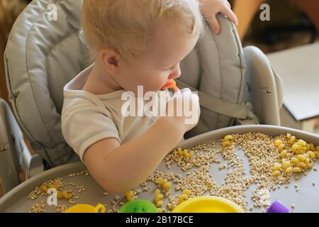 L'enfant mange des jouets qui poonent de porridge. Développement de compétences en moteurs fins chez les enfants jusqu'à l'année. Concept développement précoce. Jouets naturels Banque D'Images