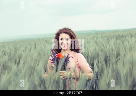 Jeune belle fille femme dans un champ tenant bouquet bouquet de fleurs de pavot et de lavande souriant, en regardant votre appareil photo. Banque D'Images