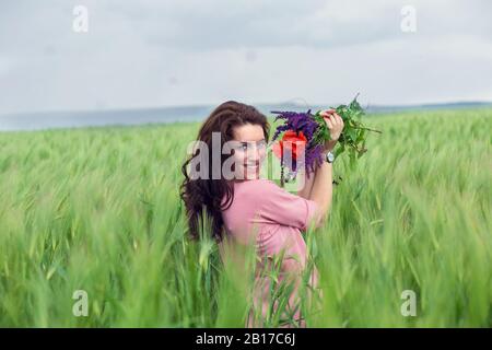 Fille profitant de la vie été dans un champ de blé avec bouquet de fleurs de pavot et de lavande. Expression positive du visage Banque D'Images