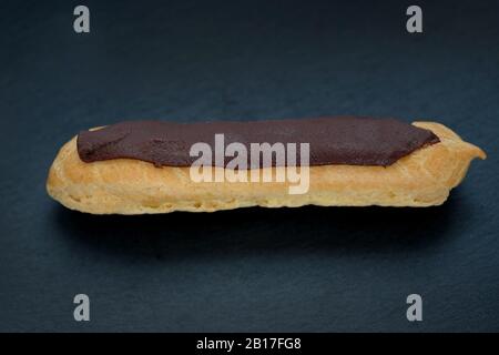 gâteau aux éclairs farci sur fond noir. eclair maison recouvert d'une bande de chocolat. Banque D'Images