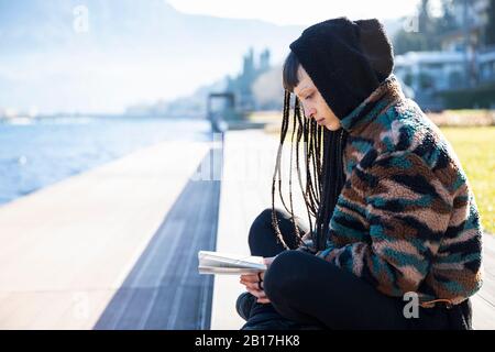 Jeune femme assise en banc de lecture d'un livre au lac de Côme, Côme, Italie Banque D'Images