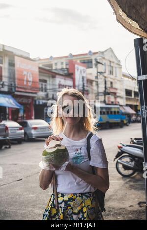 Portrait d'une femme souriante buvant de la noix de coco, la vieille ville de Phuket, Thaïlande Banque D'Images