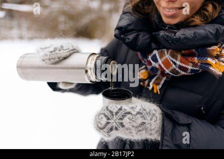 Vue sur la récolte d'une femme qui verse du thé dans un mug thermo en hiver Banque D'Images