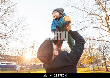 L'homme lève son heureux fils de bébé au parc Banque D'Images