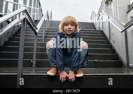 Portrait de garçon blond rouching sur les escaliers à l'extérieur Banque D'Images