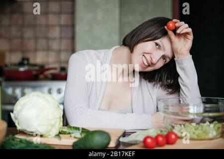 Portrait d'une heureuse femme préparant la salade dans la cuisine Banque D'Images