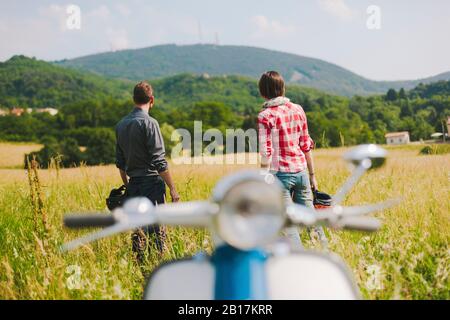 Vue arrière d'un couple avec scooter de voiture vintage debout sur un pré profitant de la vue, Toscane, Italie Banque D'Images