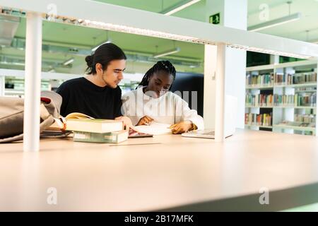 Deux étudiants avec ordinateur portable et livres d'apprentissage dans une bibliothèque Banque D'Images