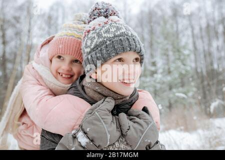 Portait de garçon donnant à sa petite sœur un tour de piggyback dans la forêt d'hiver Banque D'Images