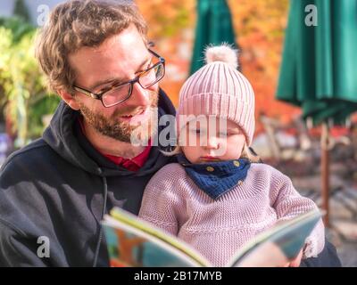 Portrait du père et de la jeune fille livre de lecture au café extérieur en automne Banque D'Images