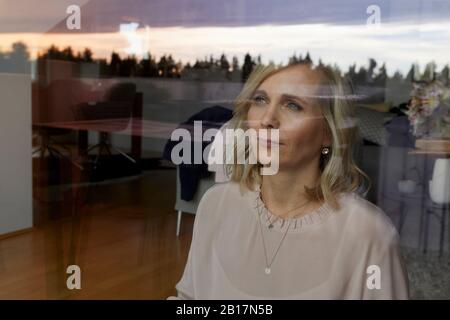 Portrait de femme blonde derrière le panneau de fenêtre à la maison Banque D'Images