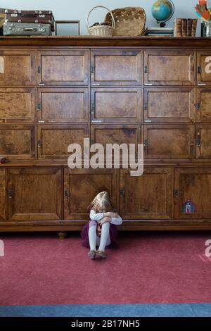 Petite fille mécontente assise sur le sol devant le grand cabinet Banque D'Images