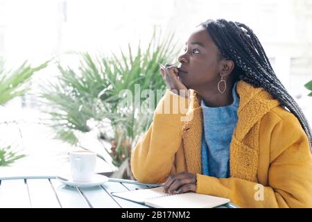 Jeune femme pensive avec carnet de notes au café pavé en regardant à distance Banque D'Images
